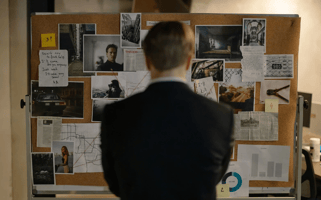  Un hombre de espaldas observa un tablero de corcho lleno de notas, fotografías y diagramas. La imagen ilustra el proceso de investigación, destacando la importancia de organizar y analizar información de manera meticulosa en la escritura de una tesis.